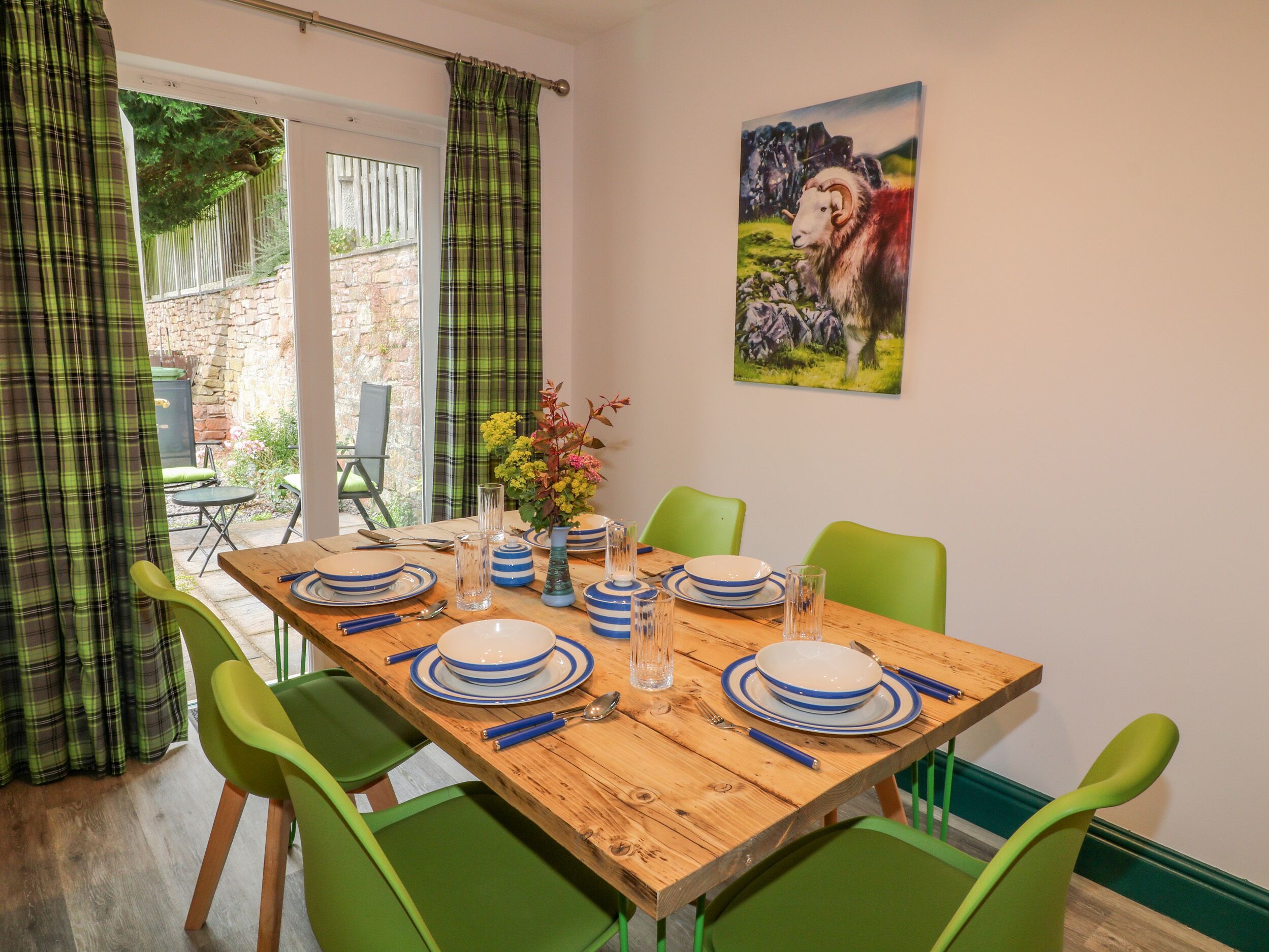 A dining area with a wooden table set for four, green chairs, and a painting of a ram on the wall.