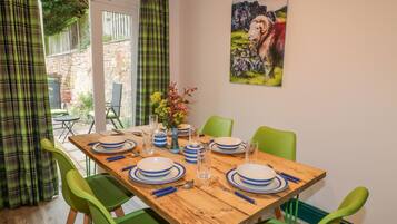 A dining area with a wooden table set for four, green chairs, and a painting of a ram on the wall.