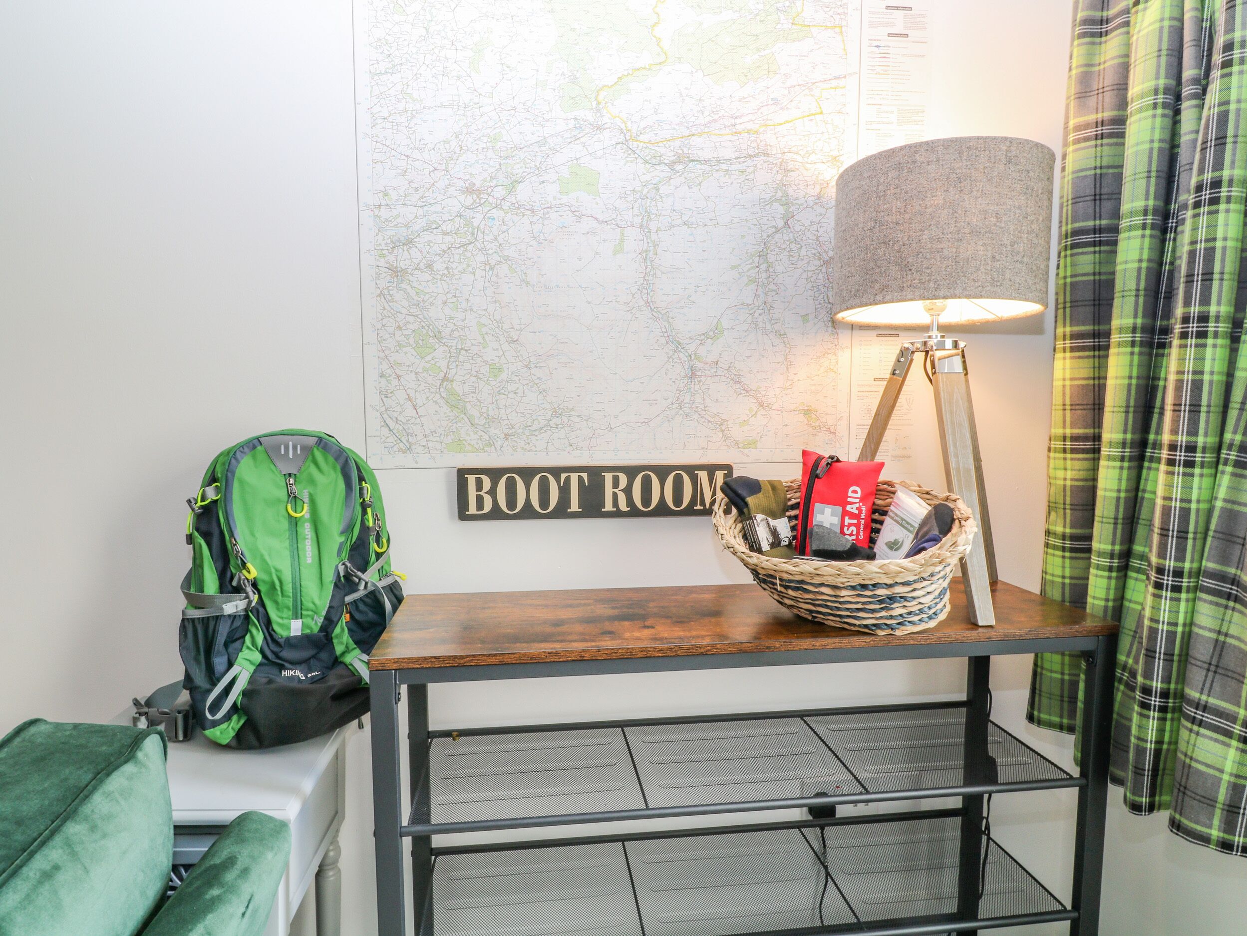 Ein Zimmer mit einer Karte, einem Schild mit der Aufschrift 'BOOT ROOM', einer Lampe, einem Korb mit Gegenständen und einem grünen Rucksack.