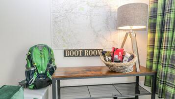 Ein Zimmer mit einer Karte, einem Schild mit der Aufschrift 'BOOT ROOM', einer Lampe, einem Korb mit Gegenständen und einem grünen Rucksack.