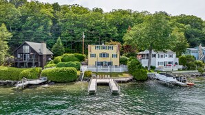 Een vakantiehuis aan het meer met een steiger, een boot en een woning met een witte gevel en groene details.