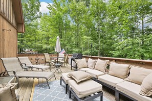 Un terrazzo in legno con mobili da esterno, tra cui un divano e delle sedie, e un barbecue.