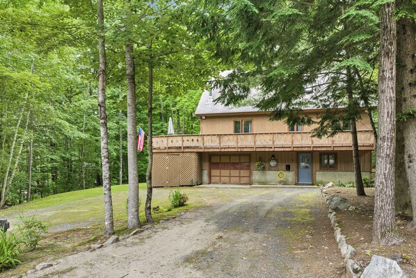 Una baita di legno con un garage, immersa tra gli alberi e con un vialetto sterrato.