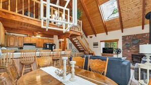 A spacious kitchen with wooden cabinets, a dining area with a wooden table and chairs, a blue sofa, and a staircase leading to an upper level.