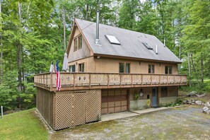 Un'abitazione di legno a due piani con un balcone, un garage e un piccolo portico.