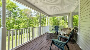 En overdækket veranda med træterrasse, hvid gelænder og siddeområde med bord og stole.