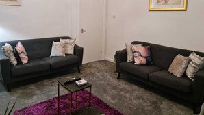 Ein Wohnzimmer mit zwei dunklen Sofas, einem kleinen schwarzen Beistelltisch und einem violetten Teppich.
