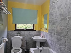 A bathroom with a toilet, sink, and bathtub. There is a window with a view of greenery outside. - Immaculate 3-bed House in Middleton (Leeds)