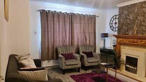 Ein Wohnzimmer mit Kamin, zwei Sesseln, einem Sofa und einem violetten Teppich.