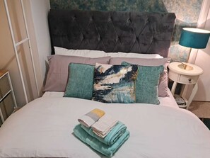 A neatly made bed with a tufted headboard, multiple pillows, and a folded towel on the bed. - Immaculate 3-bed House in Middleton (Leeds)