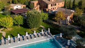 Une grande piscine, dotée de chaises longues et de parasols, entourée d’une pelouse bien entretenue et offrant une vue sur la campagne.