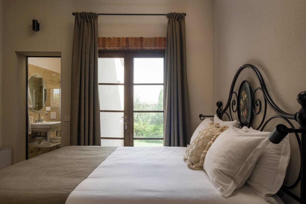 Ein Schlafzimmer mit einem großen Bett, einem Fenster mit Vorhängen, einem Nachttisch und einem Spiegel.