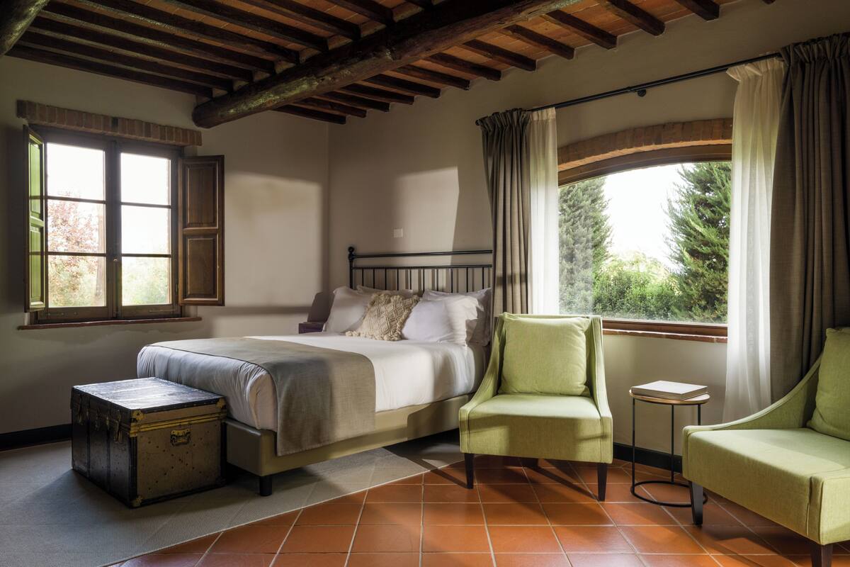 Ein Schlafzimmer mit einem Bett, zwei Stühlen, einem kleinen Tisch und einem Koffer.