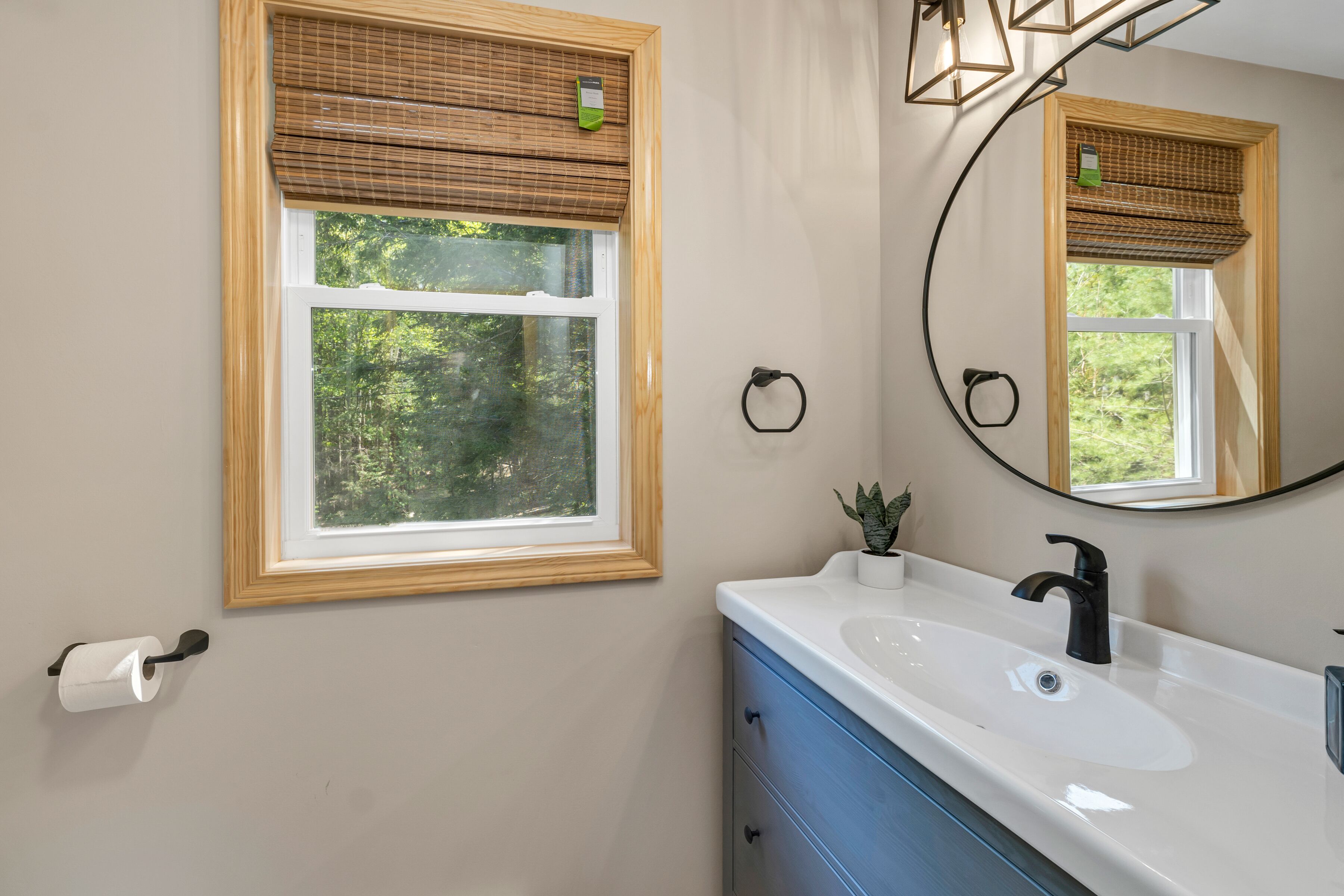 A bathroom with a window, a sink, a mirror, and a toilet paper holder.