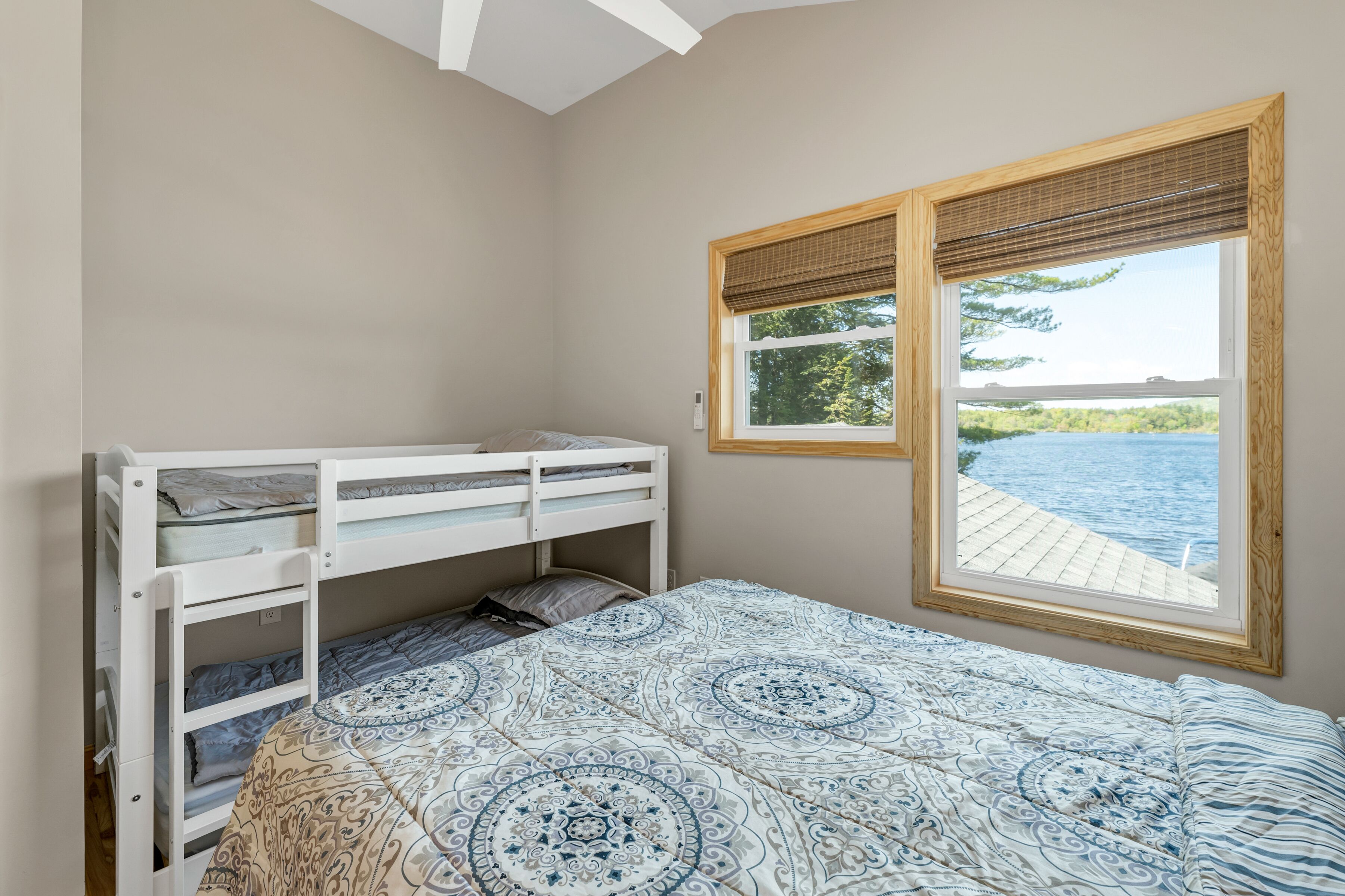 A bedroom with a bunk bed, a large window with a view of a body of water, and a patterned bedspread.
