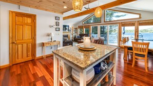 Una cocina amplia con pisos de madera, encimera de granito y una isla grande. Hay sillas de madera y una mesa de comedor con vista al lago.