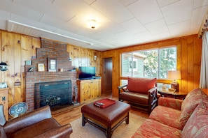 A cozy living room with a brick fireplace, wooden walls, a television, and comfortable seating.