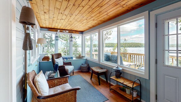 Une pièce chaleureuse avec un plafond en bois, de grandes fenêtres, des meubles en osier et une vue sur un quai.