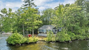 Un chalet au bord du lac, doté d’une terrasse et entouré d’une forêt dense, avec un plan d’eau paisible à proximité.