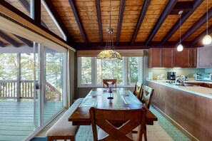 Enjoy meals in this dining area with a large table for four, surrounded by matching chairs and a high ceiling with exposed beams.