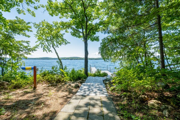 Stroll along the stone pathway to a serene lake dock, surrounded by lush greenery and rolling hills.