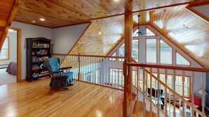 Ein geräumiges Schlafzimmer im Loft-Stil mit Holzbalkendecke, einem Schaukelstuhl, einem Bücherregal und Blick ins Freie.