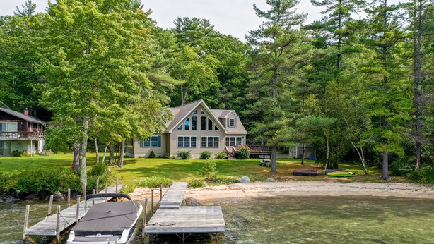 Ein Haus am Seeufer mit einer Anlegestelle, die ins Wasser führt, umgeben von dichtem Baumbestand.