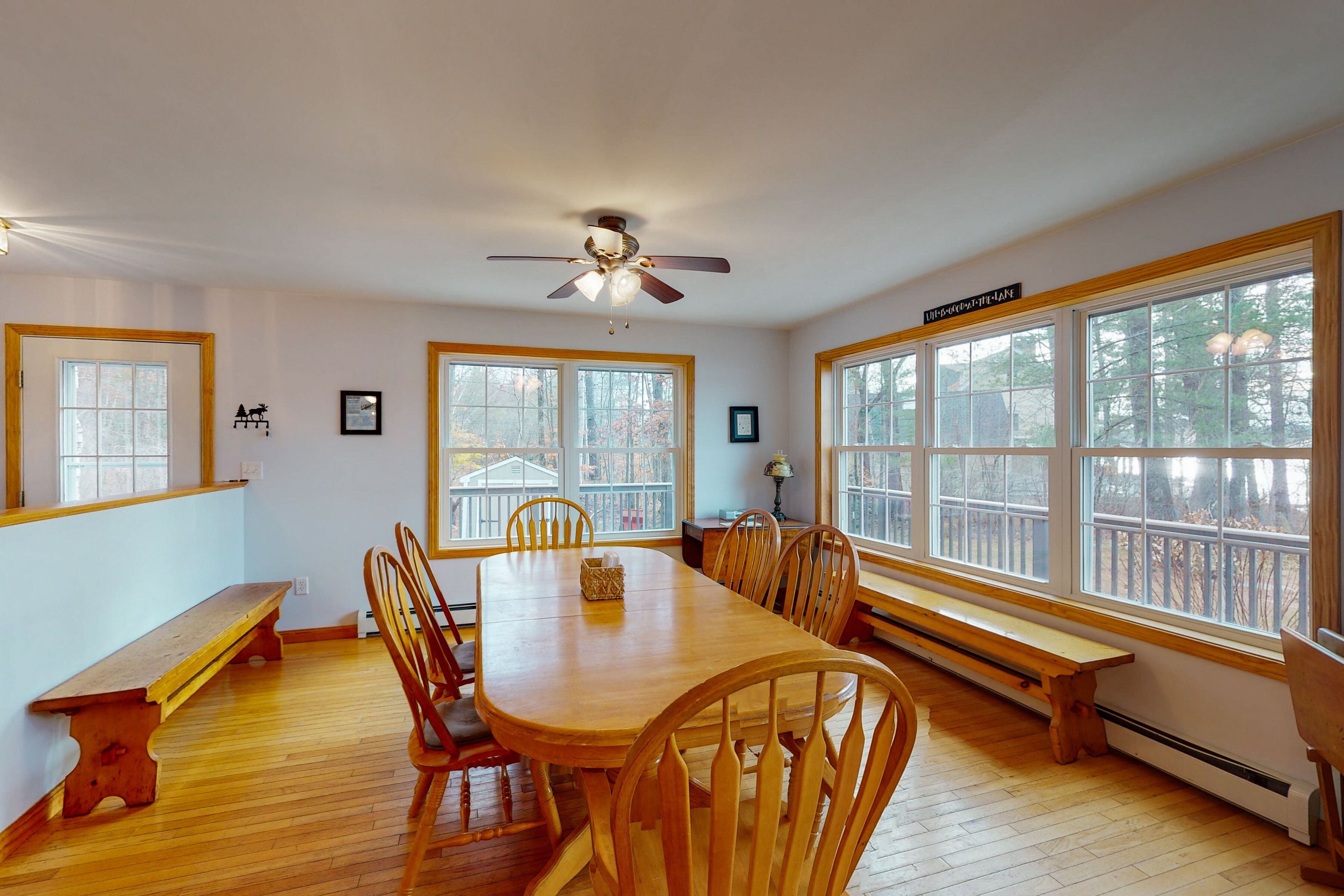 A dining room with a wooden table and chairs, large windows, and a ceiling fan.
