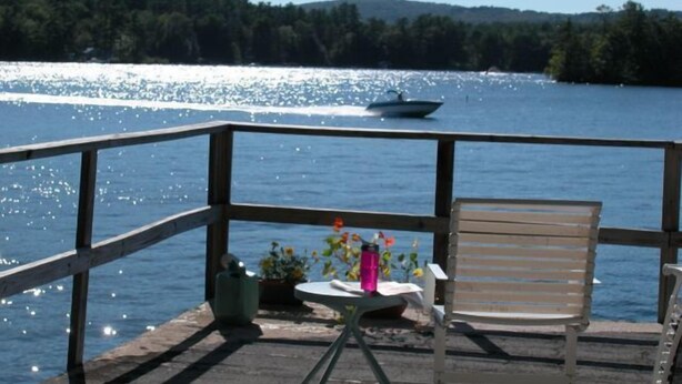 Een houten terras met een tafel en stoel met uitzicht op een meer, met een boot in de verte.