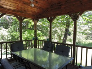 Relax in this serene outdoor seating area with a glass-top table and four cushioned chairs, surrounded by a lush forest view.