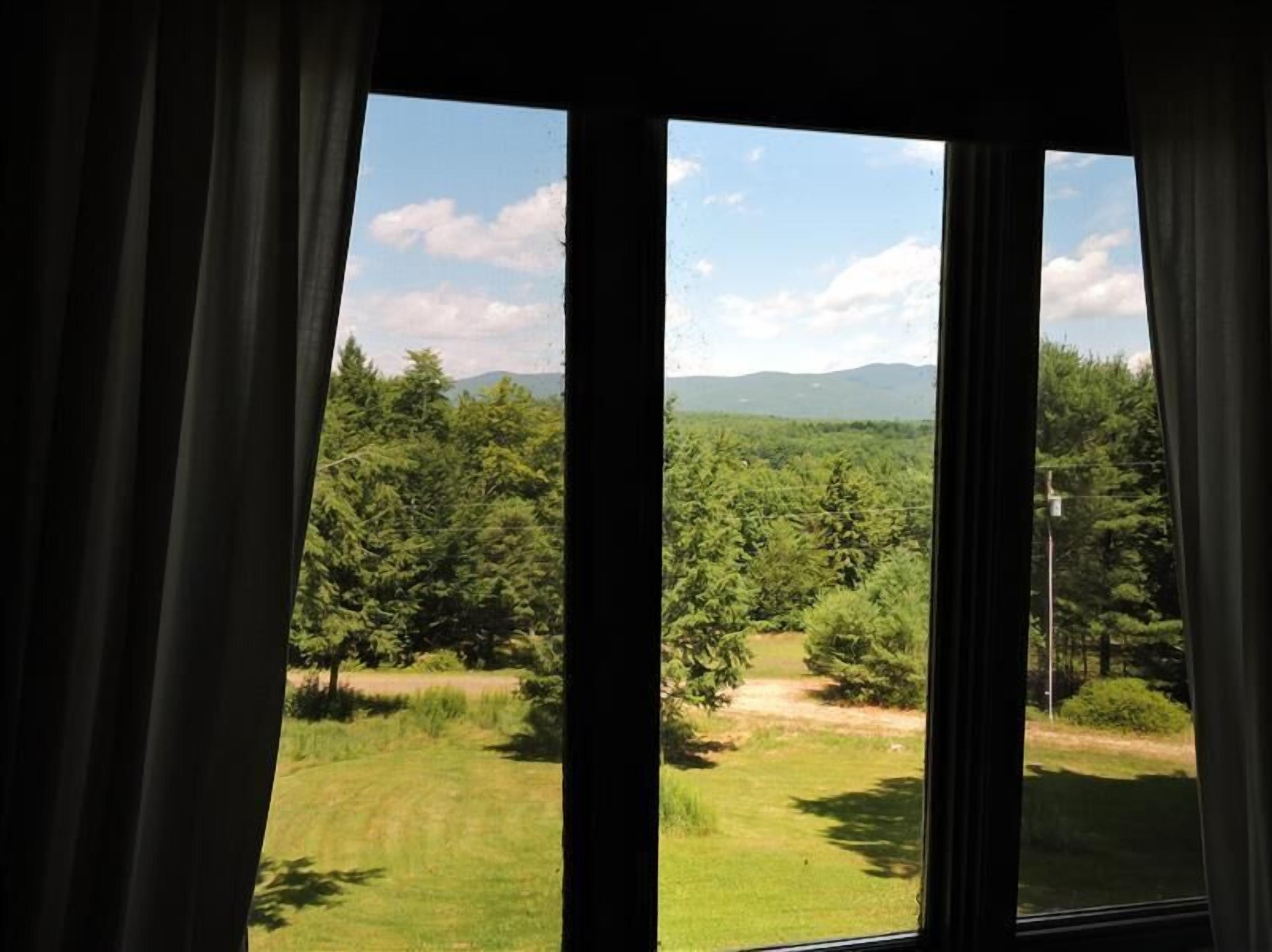 Una habitación con un amplio ventanal que da a un paisaje boscoso y montañas en la distancia.