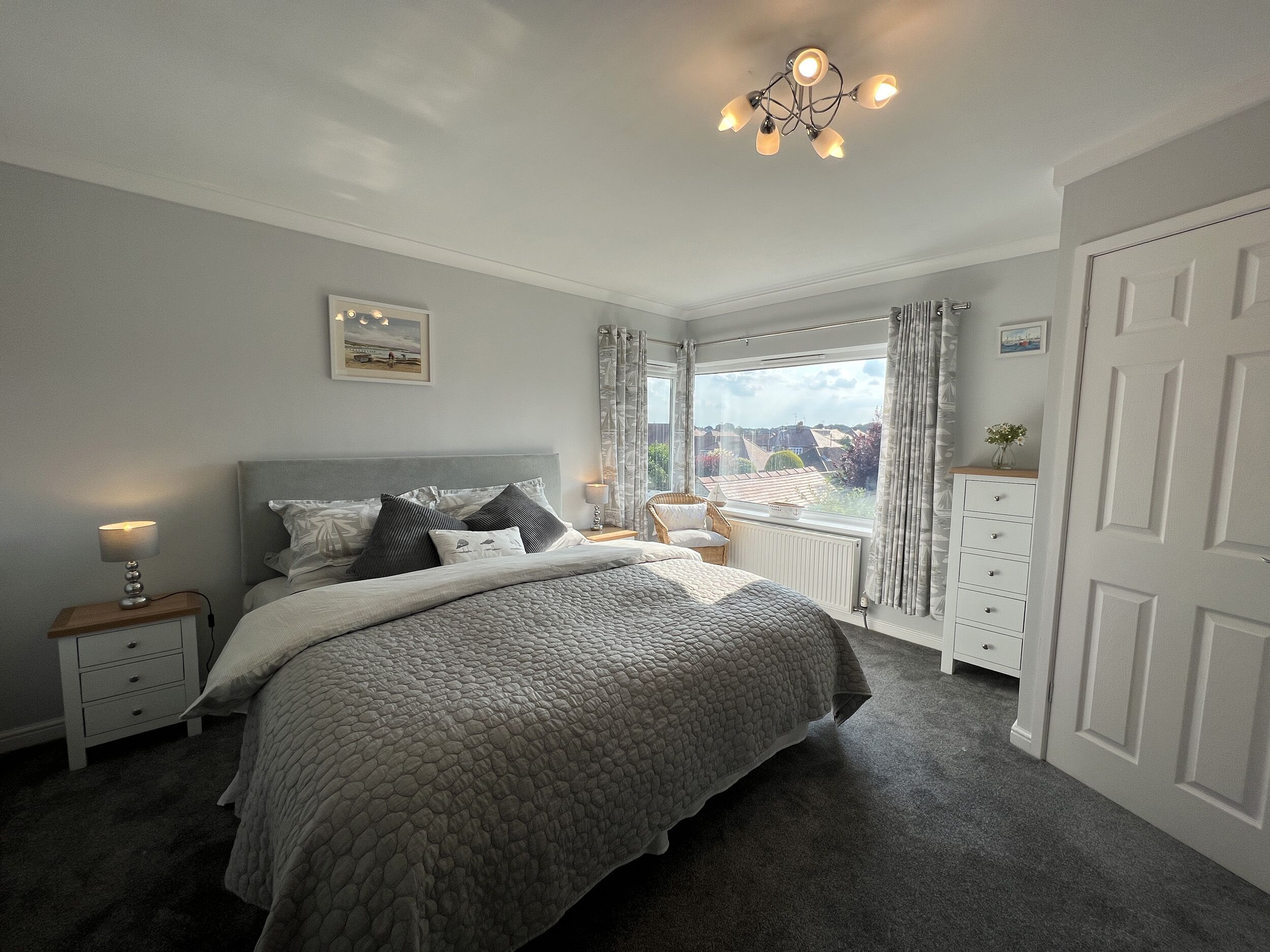 A bedroom with a bed, nightstands, a window with curtains, a radiator, and a door.