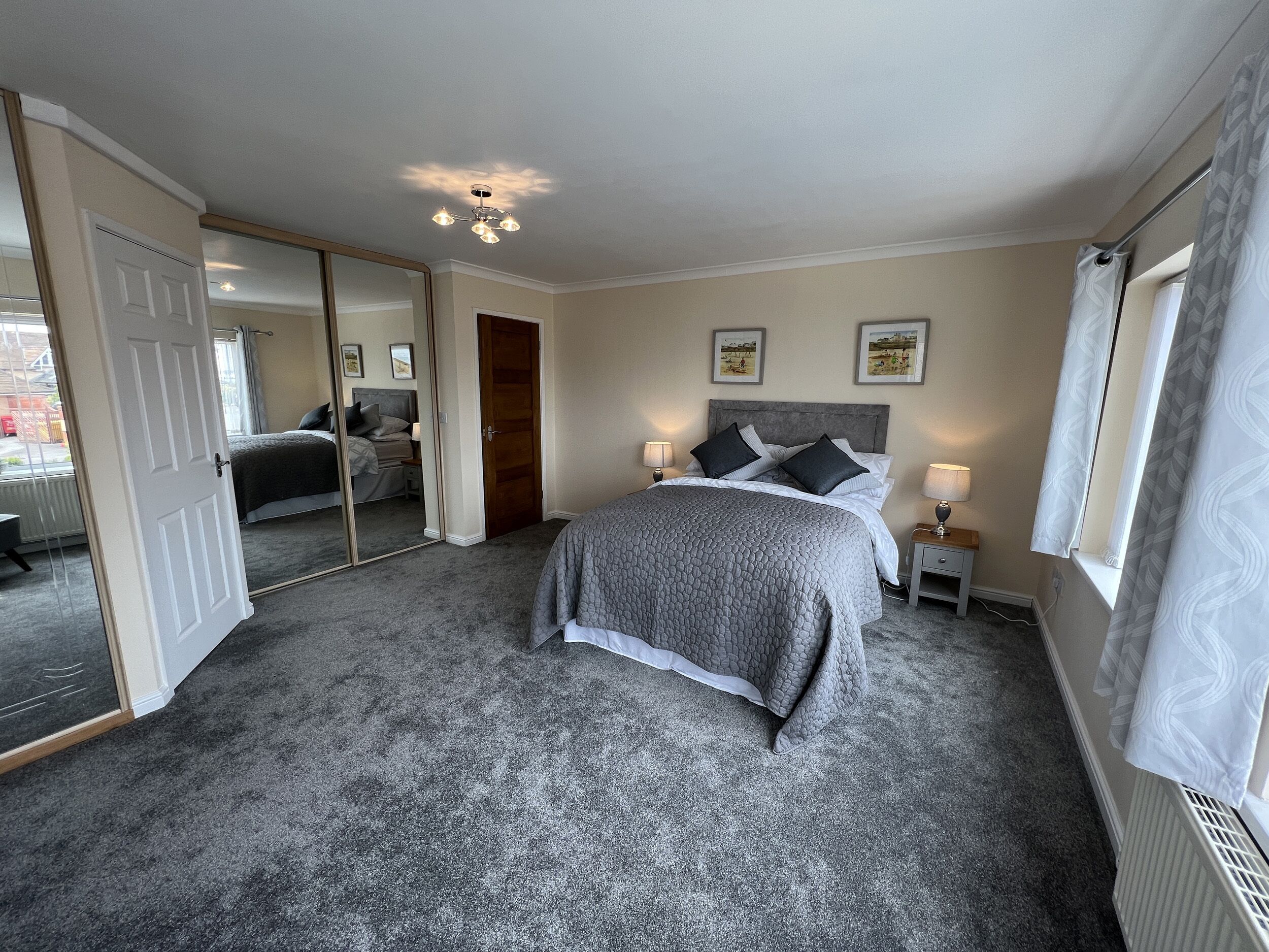 A bedroom with a large bed, bedside lamps, a mirror, and a ceiling light fixture.