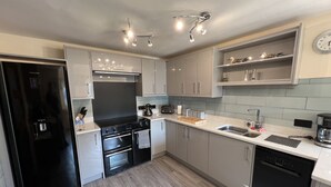 A modern kitchen with a black refrigerator, a stove, an oven, a dishwasher, and a sink. There are cabinets, a countertop, and a clock on the wall. - The Emberton (Bridlington)