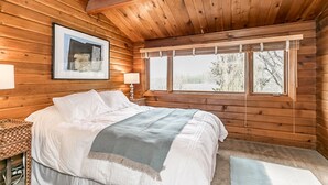 Une chambre dans un chalet en bois, avec un lit, une fenêtre avec des rideaux et un tableau encadré au mur.
