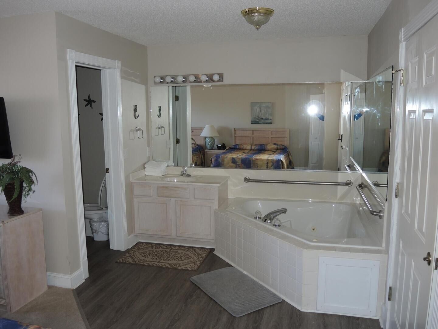 A bathroom with a large bathtub, a sink, and a mirror. There is a door leading to another room, and a rug on the floor.