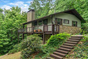 A two-story house with a stone foundation, a balcony, and a staircase leading to the entrance.