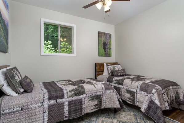 A bedroom with two beds, a window with a view of trees, and a ceiling fan.
