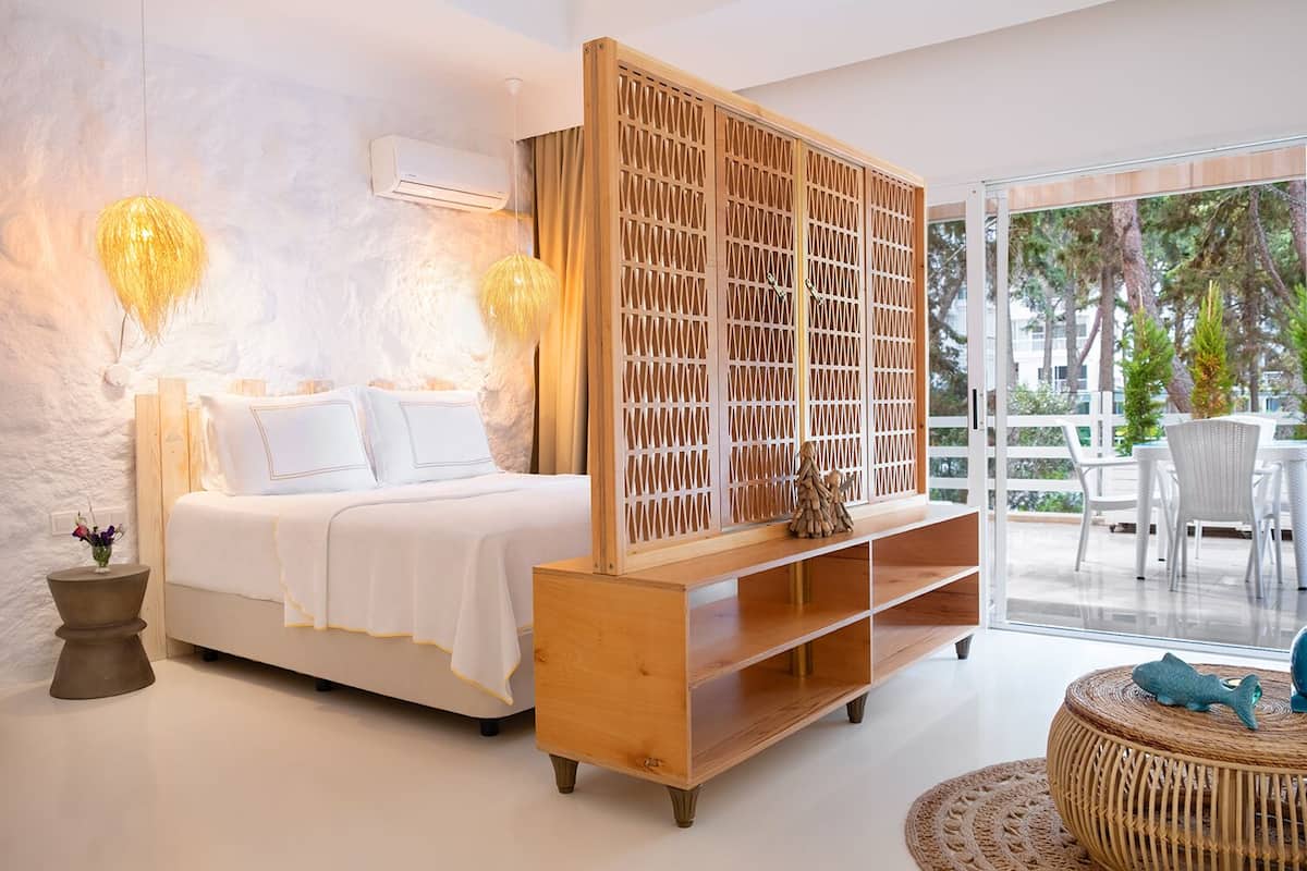Un dormitorio con cama, un mueble bajo de televisión de madera, una mesita con decoración de pez y vistas al exterior.