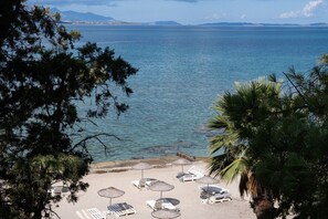 A beach with lounge chairs and umbrellas, a clear view of the sea, and distant mountains.