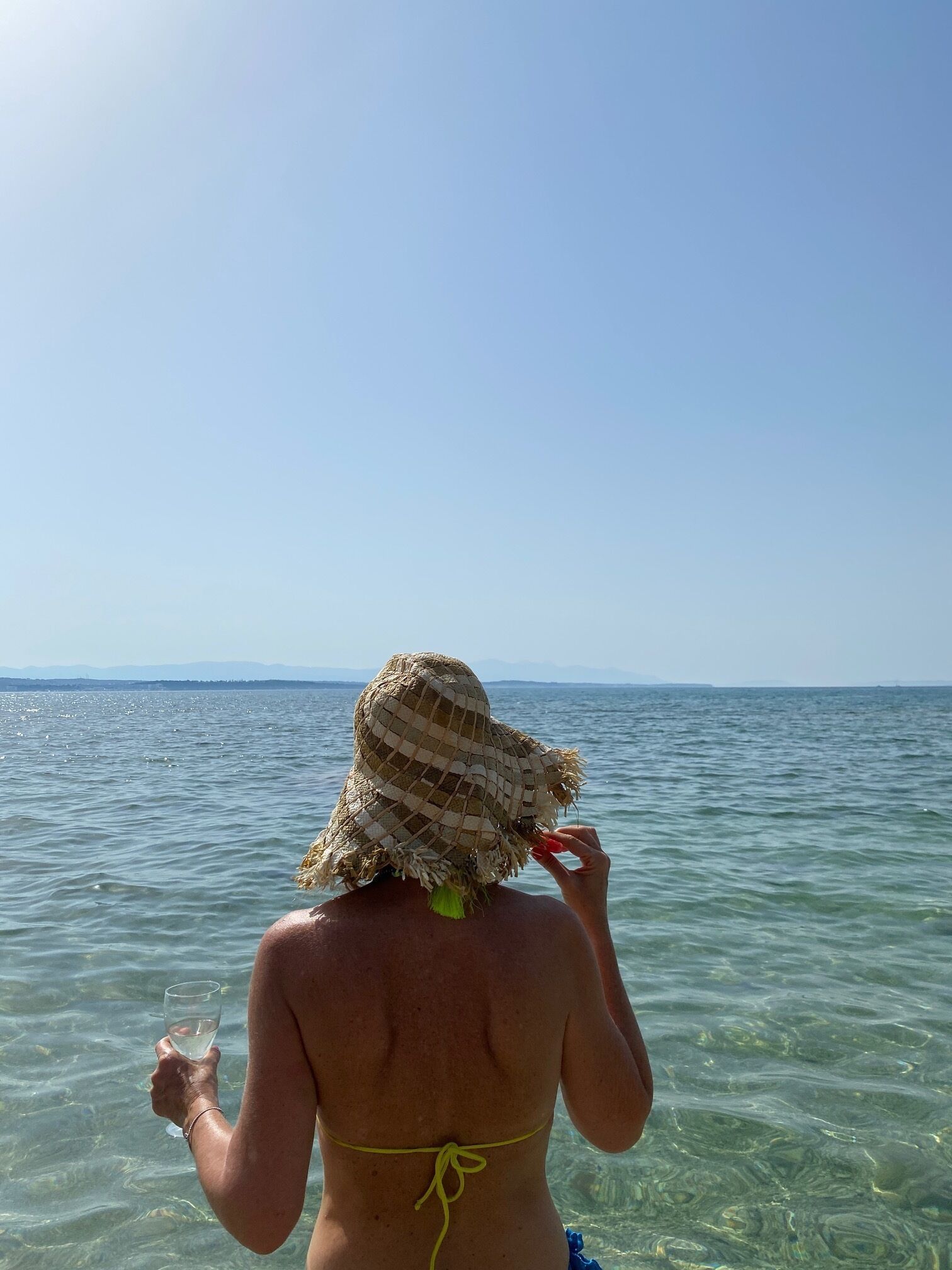 Een persoon in een bikini en strohoed die aan het water staat.