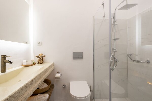 A modern bathroom with a glass shower enclosure, a marble countertop, and a white toilet.