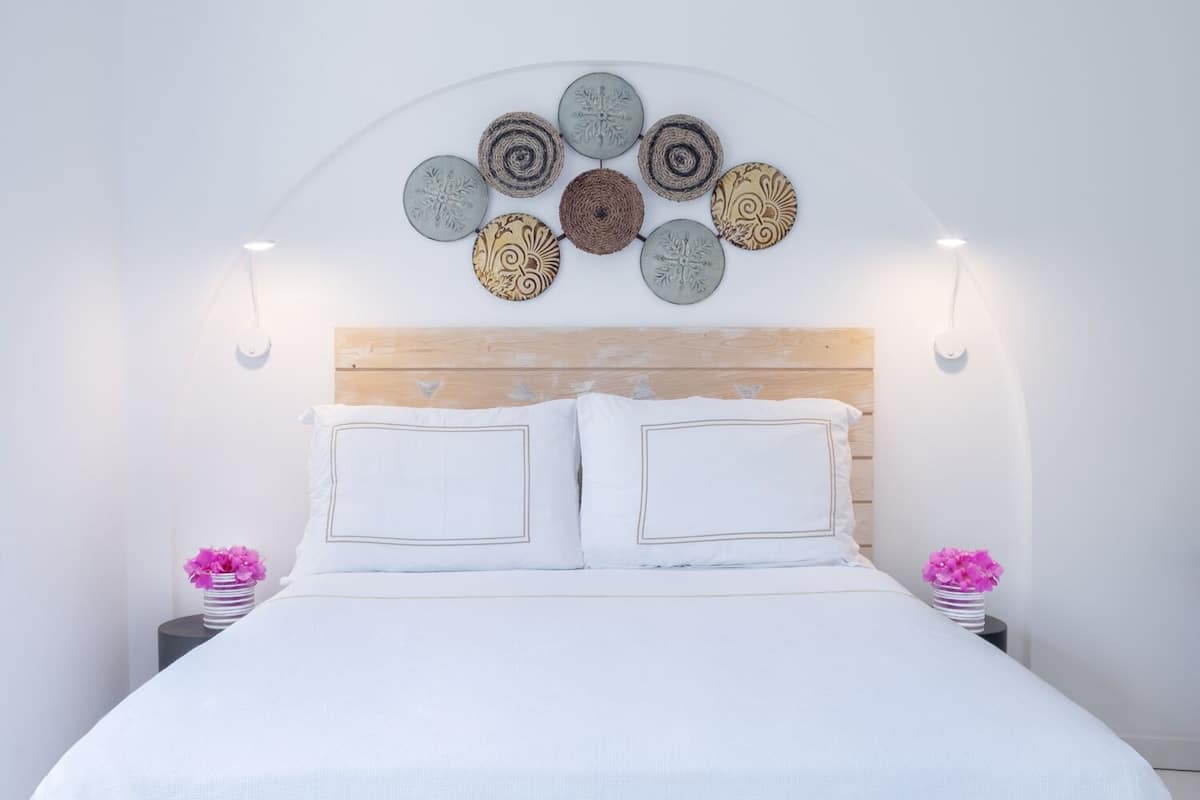 Una cama bien tendida con sábanas blancas, cabecera de madera y un arreglo decorativo de platos en la pared.