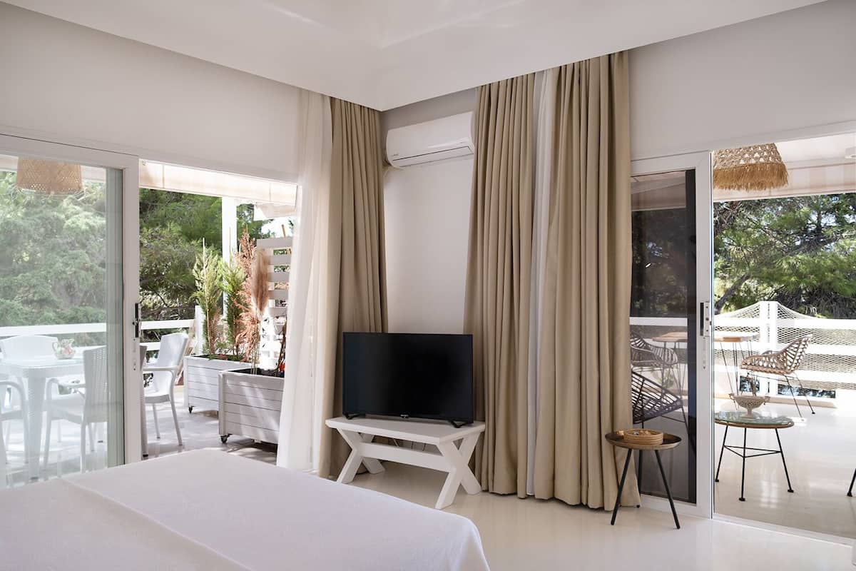 Una habitación de hotel moderna con cama, televisión y balcón con mobiliario exterior.
