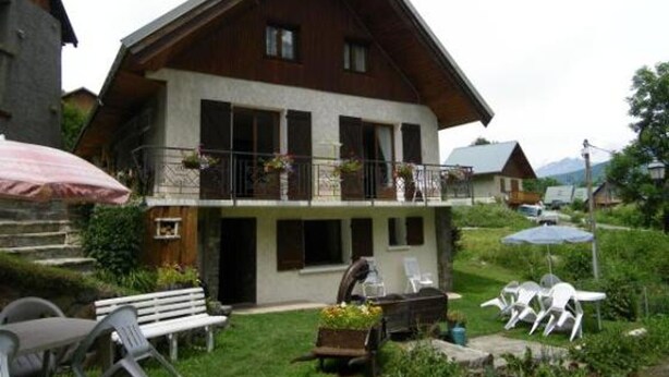 Un chalet à deux étages doté d’un balcon, d’un espace salon extérieur et d’un jardin.