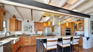 Una cocina con armarios de madera, un refrigerador de acero inoxidable, una barra con taburetes y una isla grande con un lavamanos.