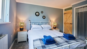 A neatly made bed with blue towels, a white headboard, and bedside lamps with patterned shades. - A Charming cottage in the Heart of Laugharne (Laugharne)
