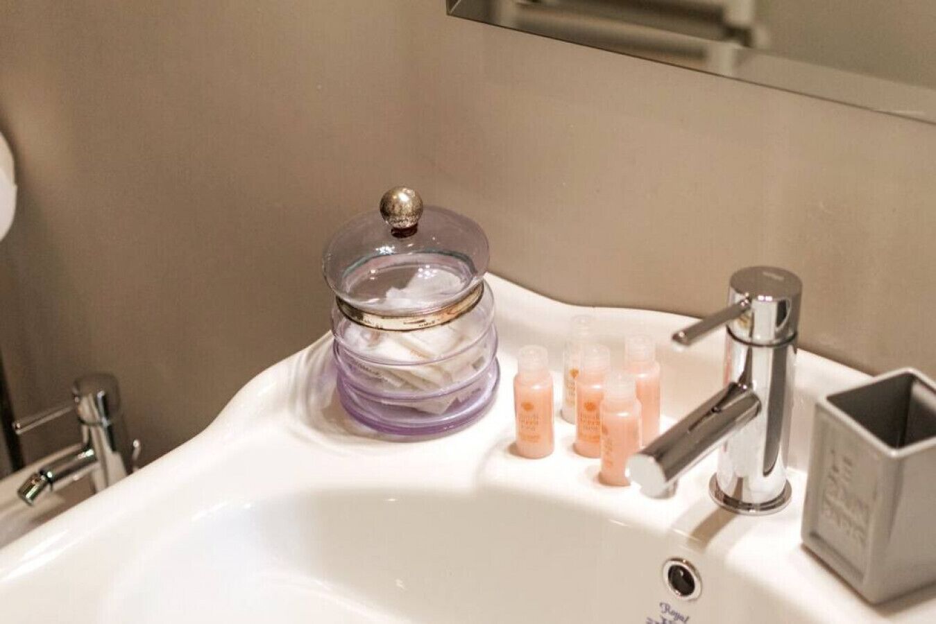 Un lavabo de baño con un tarro de vidrio que contiene un producto morado, un grifo y varias botellas pequeñas de jabón líquido.