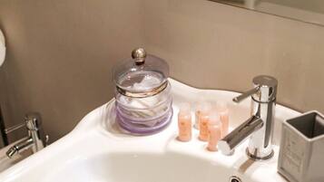 Un lavabo de baño con un tarro de vidrio que contiene un producto morado, un grifo y varias botellas pequeñas de jabón líquido.