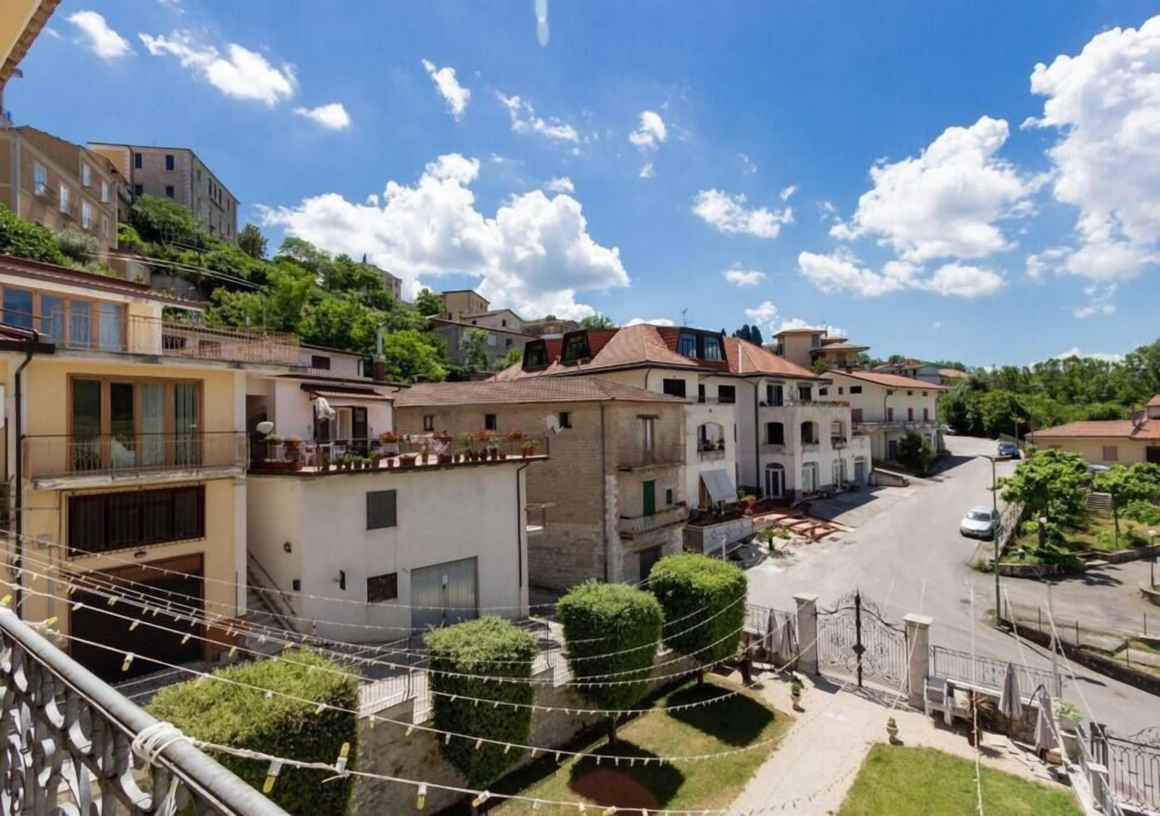 A residential street with buildings, a clear sky, and a balcony with string lights.